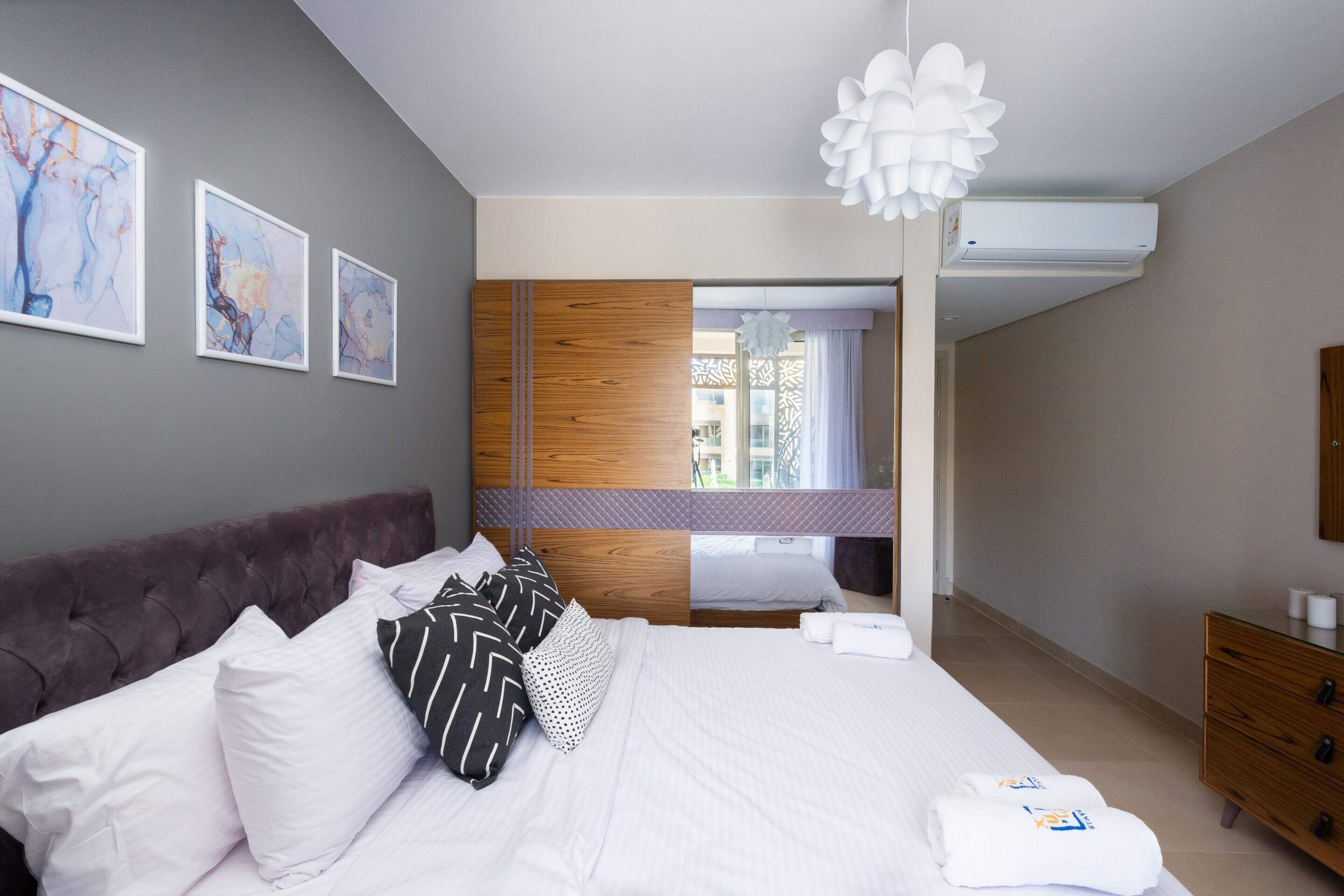 Une chambre d’hôtel moderne avec un grand lit, une armoire en bois, une coiffeuse avec un miroir et des œuvres d’art accrochées aux murs.