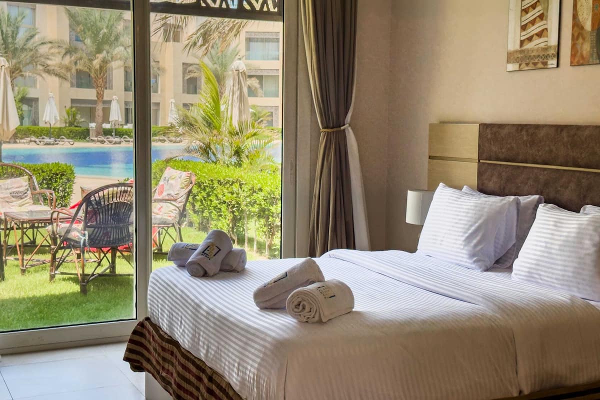 A hotel room with a bed, a view of a pool, and outdoor furniture.