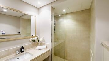 A modern bathroom with a glass-enclosed shower, a large mirror, and a sink with a towel and flowers.