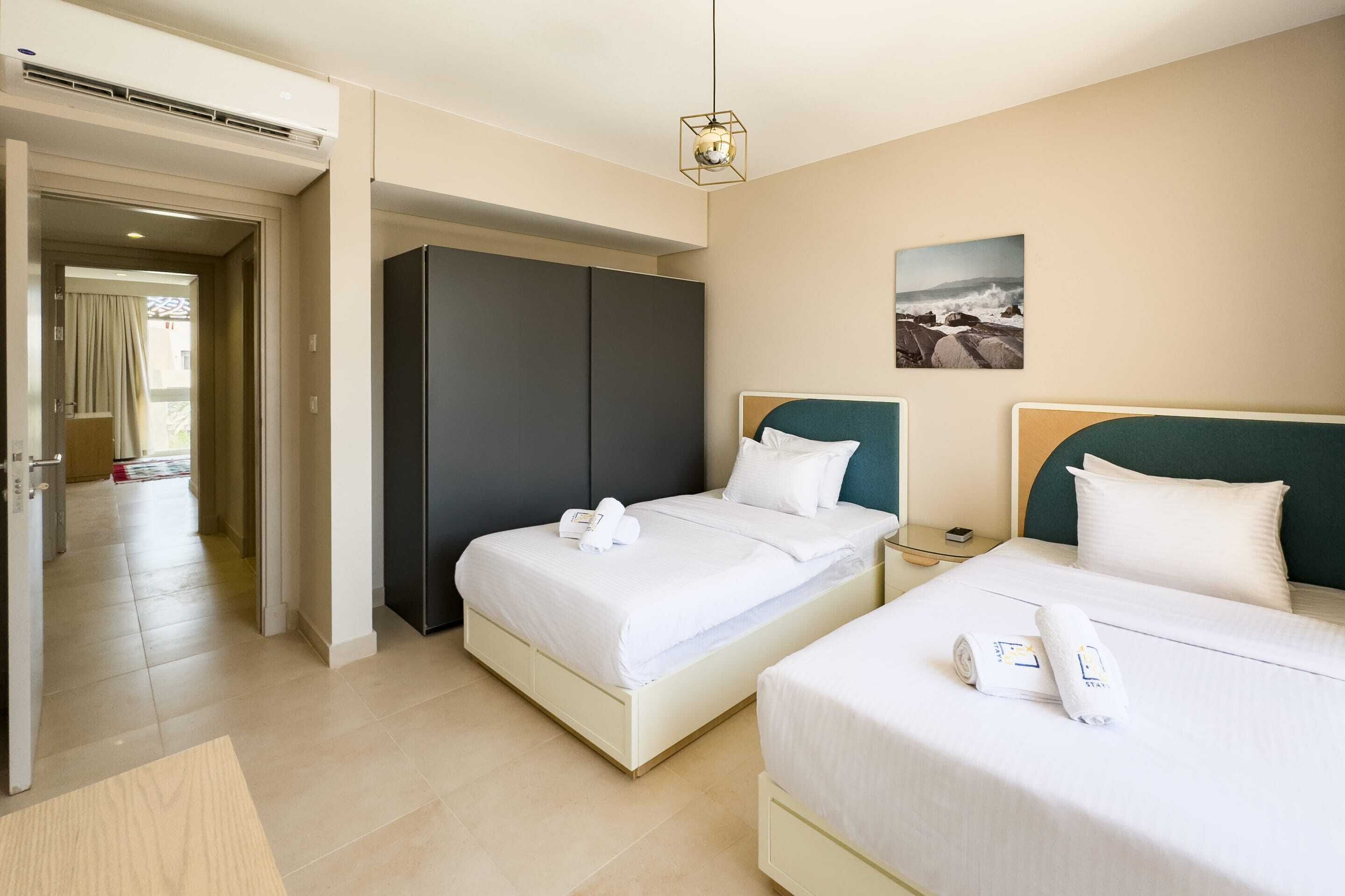 A hotel room with two beds, a wardrobe, a bedside table, and a picture on the wall.