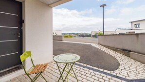 A balcony with a green chair and a small table, a black door, and a view of a paved area and buildings in the distance. - "L'escale du Goelo" in Paimpol, close to beaches (Paimpol)