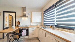 A modern kitchen with a wooden table, black chairs, a built-in oven, and a window with blinds. - "L'escale du Goelo" in Paimpol, close to beaches (Paimpol)
