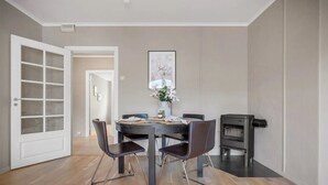 A dining area with a round table, four chairs, a vase with flowers, and a wood-burning stove.