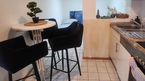 A compact kitchenette with a small dining area, a potted plant, and a view of a bedroom.