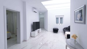A modern interior with a TV on a stand, a sofa, a small table with a vase, and a ceiling light. - Home in Las Palmas Near Las Canteras Beach (Las Palmas de Gran Canaria)