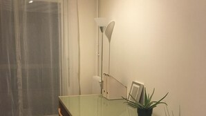 Une petite pièce bien éclairée, avec une table à plateau de verre, une seule chaise, une plante en pot et un lampadaire.