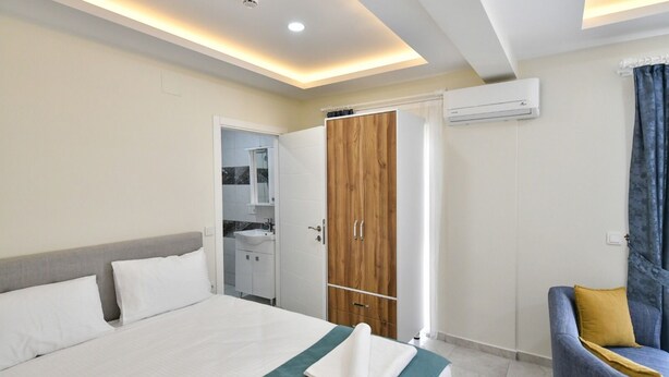 A modern hotel room with a bed, a wooden wardrobe, a bathroom with a mirror, and a seating area with a chair and a sofa. - Lamira Pansion (Fethiye)