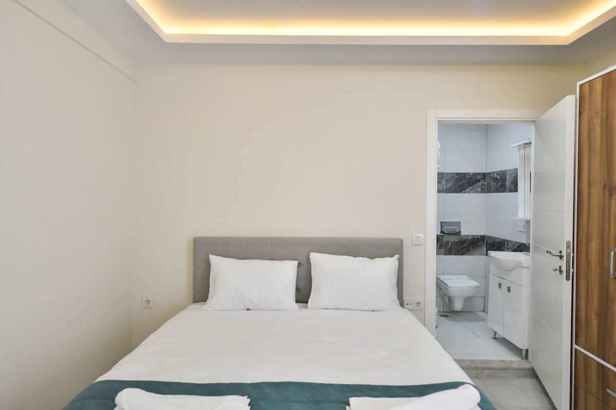 A bedroom with a bed, a bedside table, and a bathroom visible through an open door.