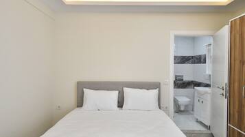 A bedroom with a bed, a bedside table, and a bathroom visible through an open door.