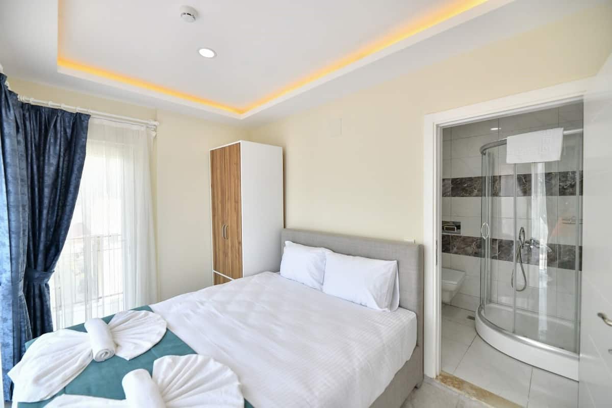 A hotel room with a bed, a wardrobe, a shower, and a window with curtains.