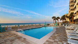 A pool area with a view of the ocean, surrounded by lounge chairs and palm trees. - Sandy Key 213:  2 BR/2 BA Perdido Key Beachfront Condo & Pools, On-Site Rental Office, Sleeps 6 (Pensacola)