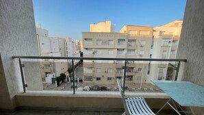 Un balcon avec une rambarde en métal, une chaise pliante blanche et une petite table.
