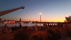 Een uitzicht op het water met een menigte mensen, een reuzenrad en een grote, verlichte constructie op de achtergrond.