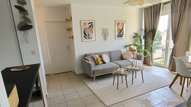 A modern living room with a grey sofa, two side tables, a coffee table, and a dining area with a white chair. - The racing n est, comfortable 2 bedroom apt, balcony, close to circuit (Le Mans)