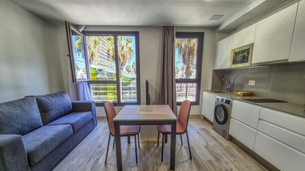 A compact living space with a sofa, dining table, chairs, a washing machine, and a kitchen area. - Apartment by Playa de Las Canteras Beach (Las Palmas de Gran Canaria)