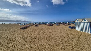 A beach with blue and white striped beach huts, sandy beach, and a clear sky. - Apartment in Las Palmas by Playa de Las Canteras (Las Palmas de Gran Canaria)