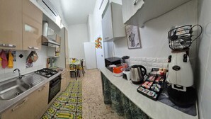 Una cocina estrecha con estufa a gas, lavamanos y cafetera. Hay una pequeña mesa de comedor con sillas.