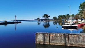 A calm waterfront with a wooden dock, boats, and a lighthouse in the distance. - Rental of a villa with swimming pool, close to the lake and ocean beaches. (Lacanau)