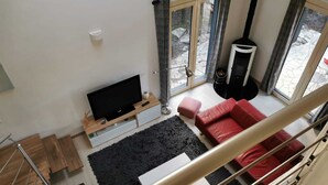 A modern living room with a flat-screen TV, a red sofa, a black rug, and a fireplace. - Rental of a villa with swimming pool, close to the lake and ocean beaches. (Lacanau)