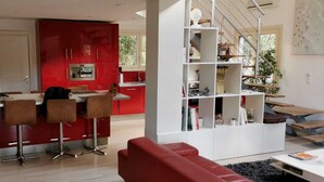 A modern living room with a red sofa, a white coffee table, and a red dining area with bar stools. - Rental of a villa with swimming pool, close to the lake and ocean beaches. (Lacanau)