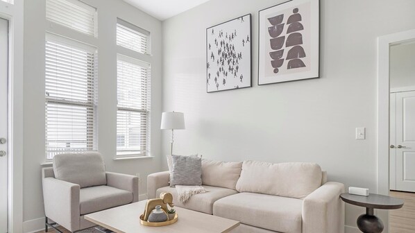 Un salon moderne avec un canapé beige, deux fauteuils, une table basse agrémentée d’objets décoratifs et des œuvres d’art accrochées au mur.