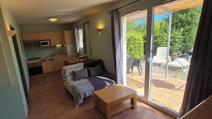 A compact living space with a kitchenette, a sofa, a small table, and a sliding glass door leading to an outdoor area. - Vacation residence with garden and 2 swimming pools. Ideal for summer vacations. (Tourrettes)