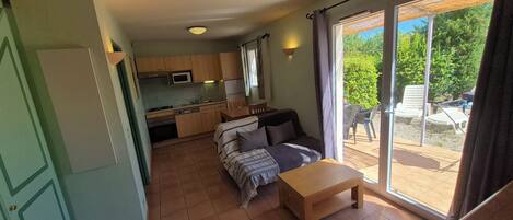 A compact living space with a kitchenette, a sofa, a small table, and a sliding glass door leading to an outdoor area.