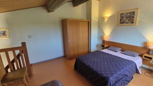 A bedroom with a bed, wooden wardrobe, two bedside tables with lamps, a chair, and a painting on the wall. - Vacation residence with garden and 2 swimming pools. Ideal for summer vacations. (Tourrettes)