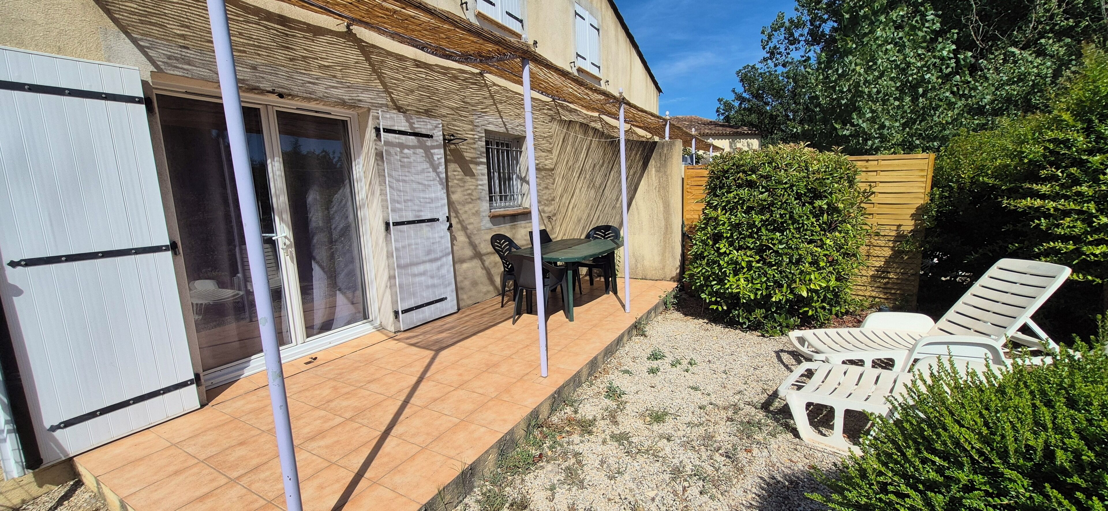 A covered patio with a table and chairs, a small garden area with gravel, and a wooden fence.