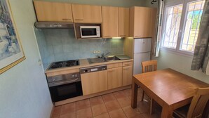 A compact kitchen with wooden cabinets, a microwave, a sink, a stove, and a dishwasher. There is a wooden table and a chair. - Vacation residence with garden and 2 swimming pools. Ideal for summer vacations. (Tourrettes)