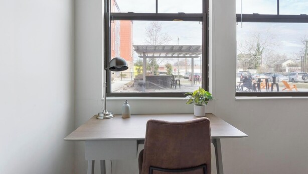 A workspace with a desk, chair, lamp, and potted plant by a window.