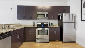 A modern kitchen with dark cabinets, stainless steel appliances, granite countertops, and a wooden floor.