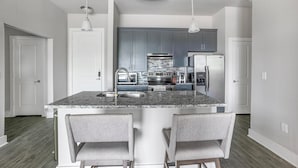 Una cocina moderna con encimeras de granito, electrodomésticos de acero inoxidable y una isla central con taburetes de bar.