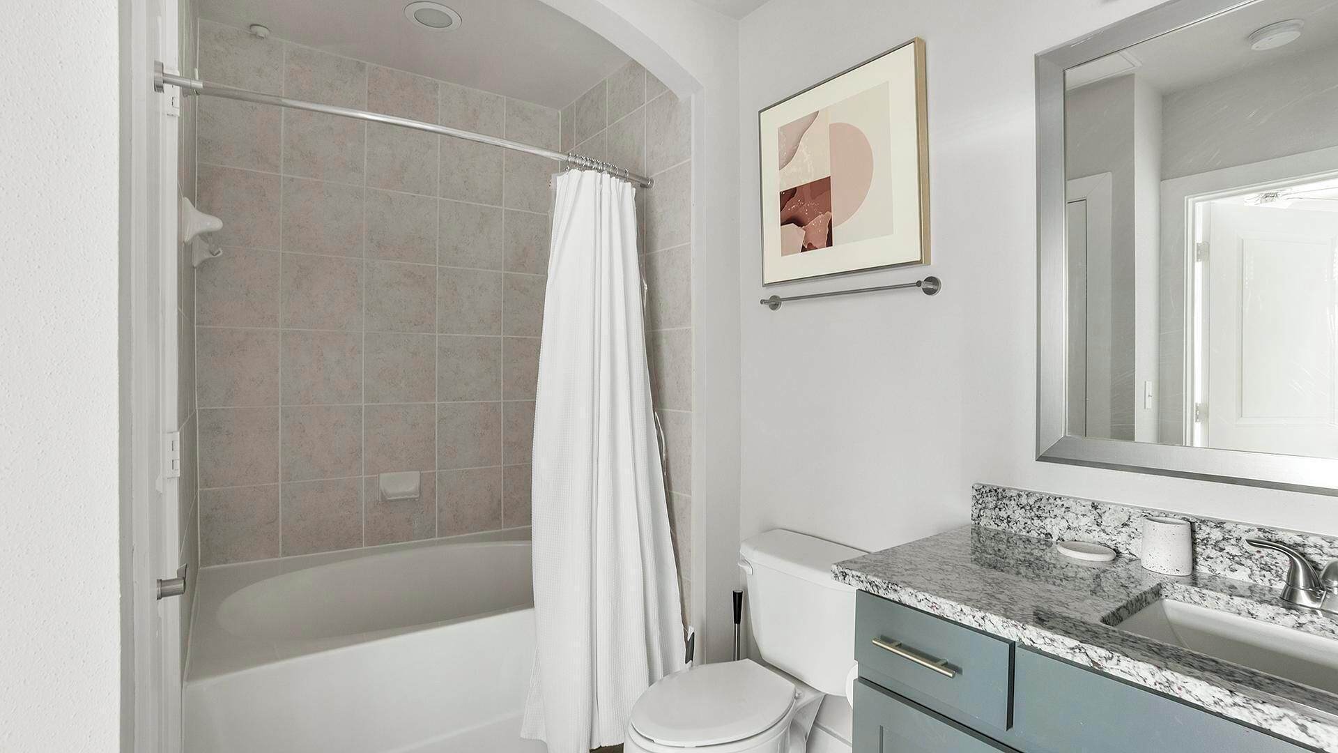 A bathroom with a shower, toilet, sink, and a framed picture on the wall.
