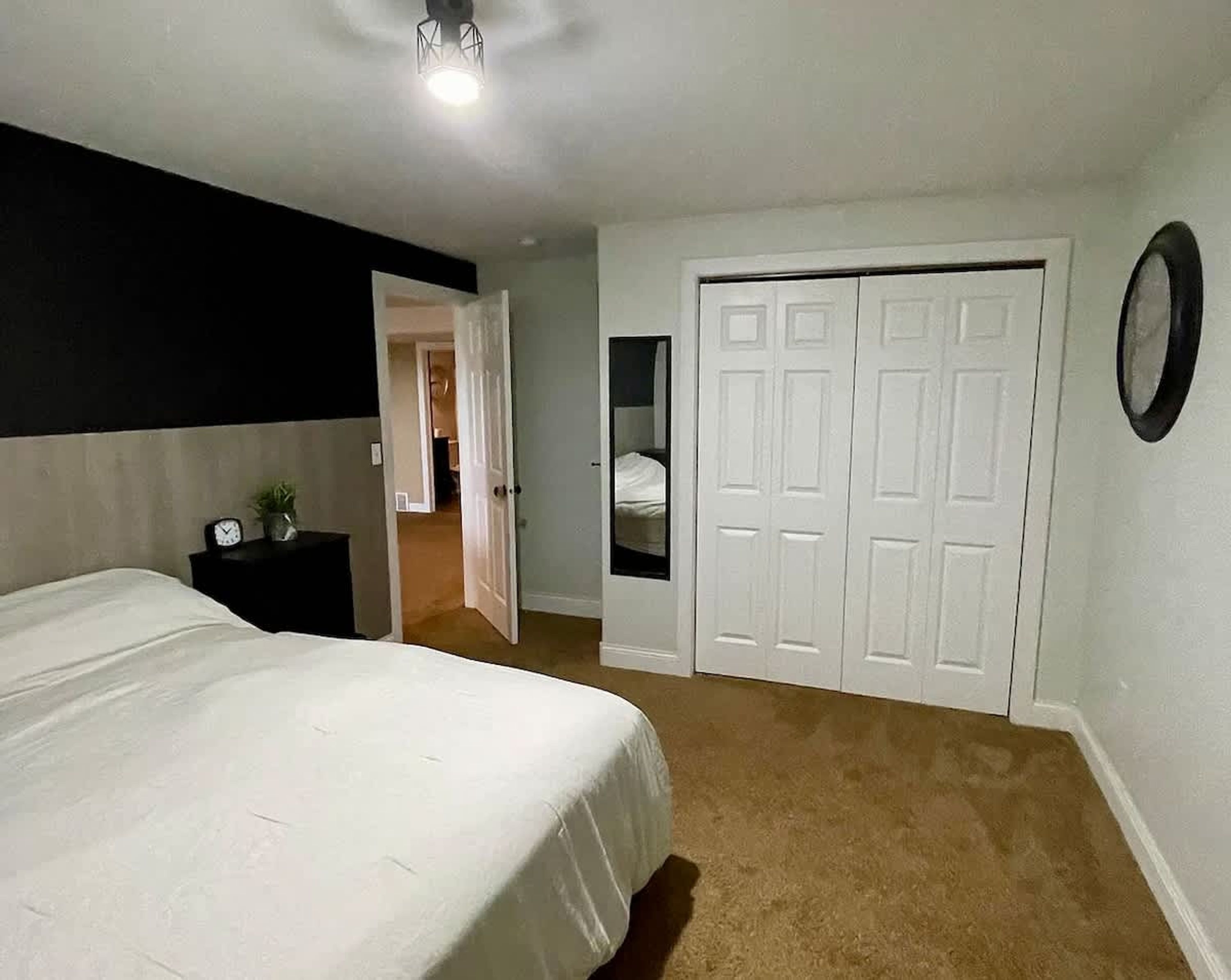 A bedroom with a bed, a nightstand, a closet, and a door leading to another room.