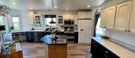 A modern kitchen with a central island, white cabinetry, and a large window providing natural light.