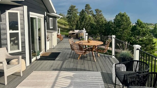 A deck with a round table and chairs, a hot tub, and a view of a forested area. - Black Hills Getaway With Hot Tub Game Room for 18 (Spearfish)