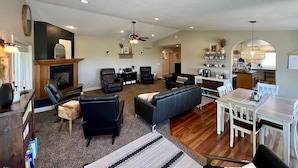 A spacious living room with a fireplace, leather sofas, a dining area with a wooden table and chairs, and a kitchen in the background. - Black Hills Getaway With Hot Tub Game Room for 18 (Spearfish)