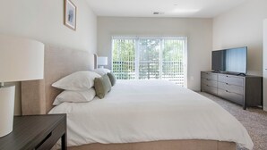Une chambre à coucher avec un lit, une télévision, une commode et une fenêtre avec des stores.