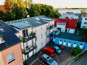 A multi-story residential building with balconies, solar panels, and a view of the water.