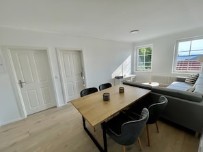 Un salon moderne avec une table à manger en bois, des chaises noires, un canapé gris et une fenêtre donnant sur un beau paysage.