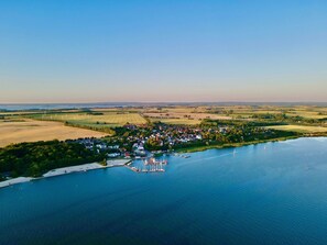 An aerial view of a lakeside village with houses, a marina, and wind turbines in the background.