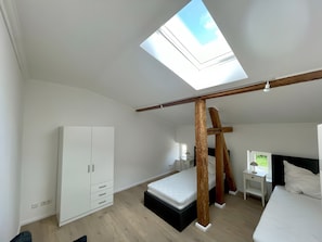 Une chambre avec un puits de lumière, une armoire, un lit et un bureau.