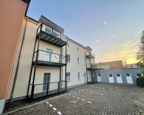 A multi-story building with a ground-level entrance, a covered outdoor area with a brick floor, and a clear sky.