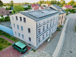Un immeuble à plusieurs étages, doté d’un toit plat, de panneaux solaires et d’un fourgon vert garé devant.