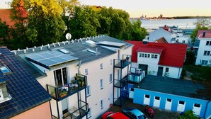 Kerrostalo, jossa on useita kerroksia, parvekkeita, aurinkopaneeleja ja näkymä vesistöön.