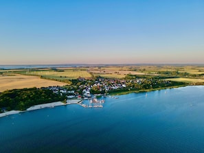 Luchtbeeld van een dorp aan een meer, met huizen, een jachthaven en windturbines op de achtergrond.