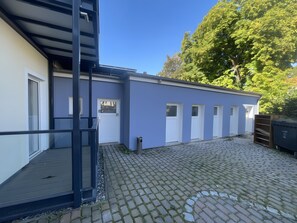 Ein Gebäude mit blauer Fassade, einer Holzterrasse und einem gepflasterten Innenhof.