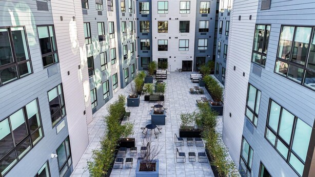 A modern building with a courtyard featuring outdoor seating and planters.