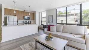 A modern kitchen with stainless steel appliances, a dining area with a white table, and a living room with a beige sofa.